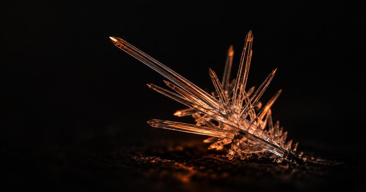 A cluster of fine needle-shaped crystals lit in orange against a near-black background