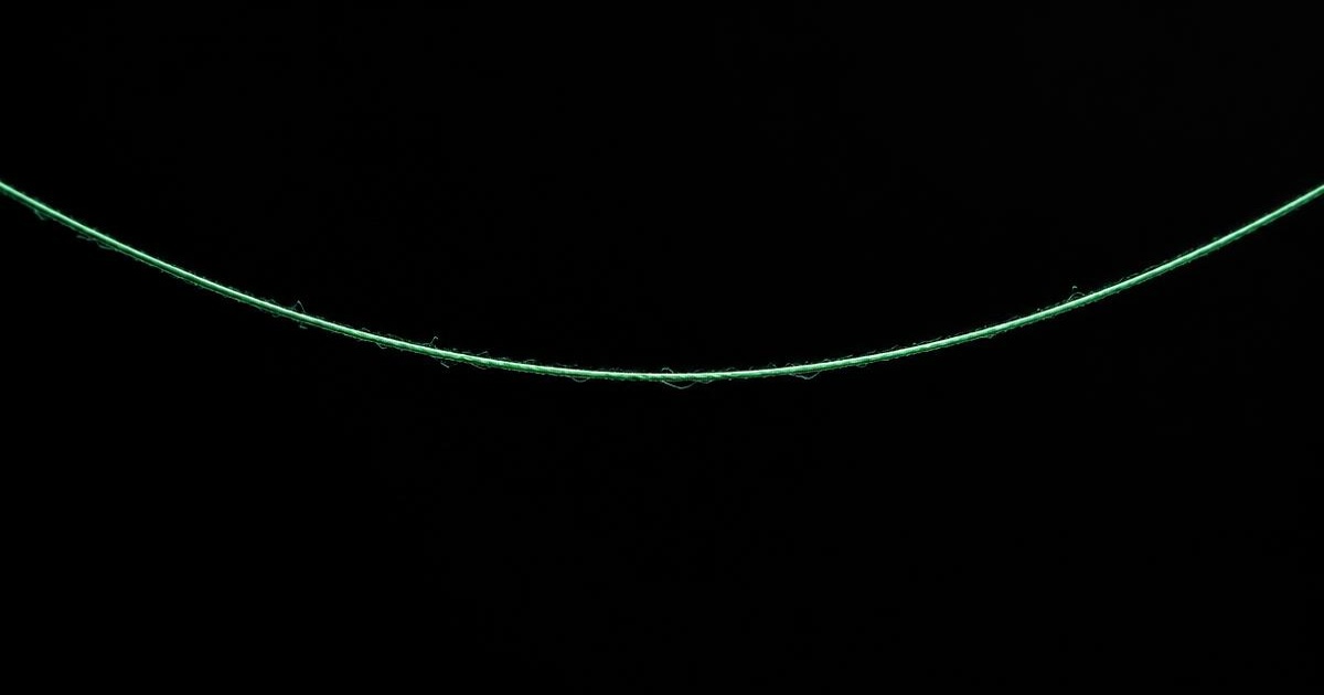 A single strand of dental floss drawn taut across a near-black background, lit in mint green